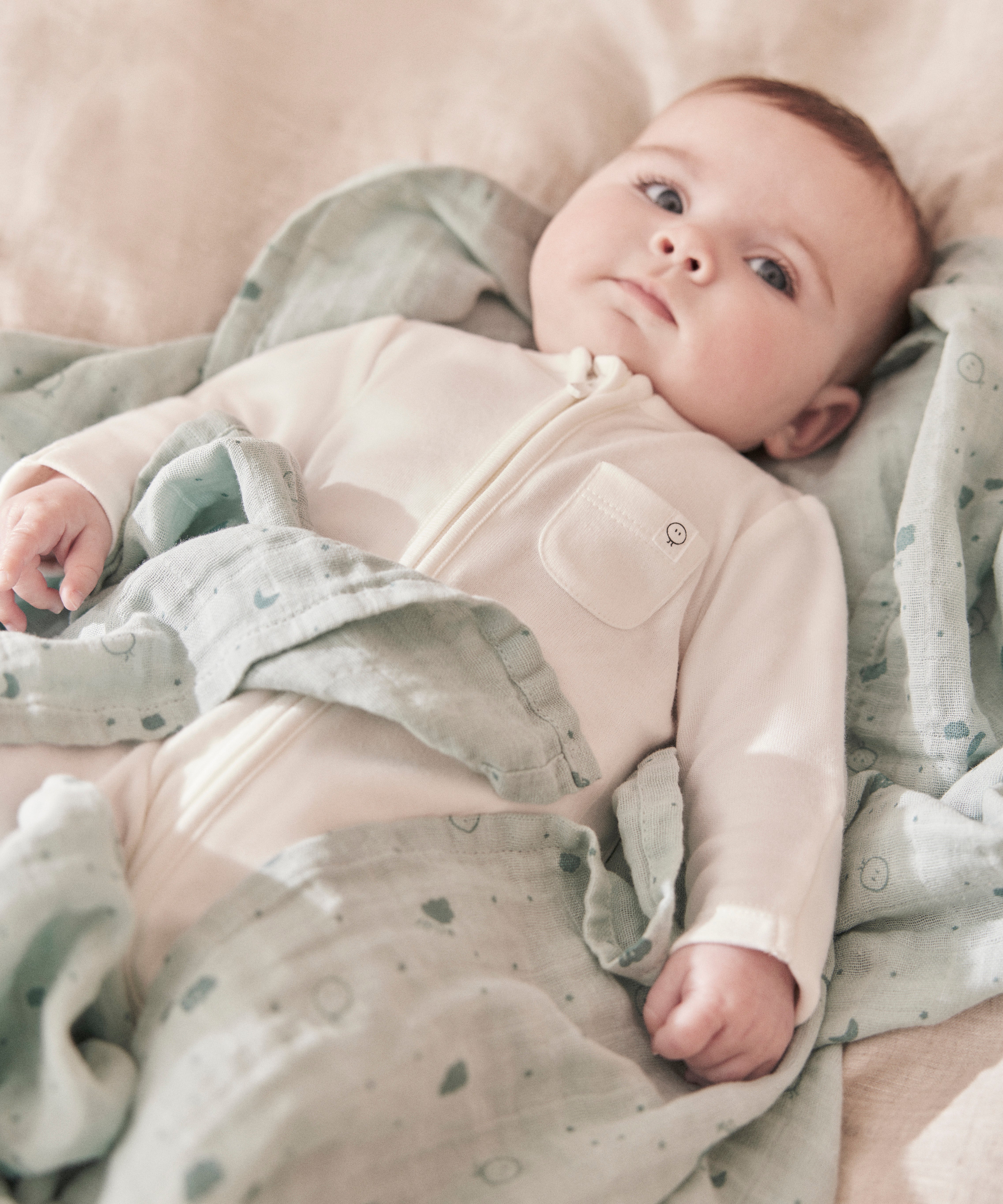 A baby lying flat on the grey MORI muslin square showing the cute dark grey prints of clouds, stars and the moon on soft organic cotton fabric