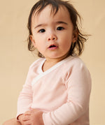 A toddler sitting down, and wearing the Mori organic cotton and bamboo blend baby kimono bodysuit in a pink blush stripe design.