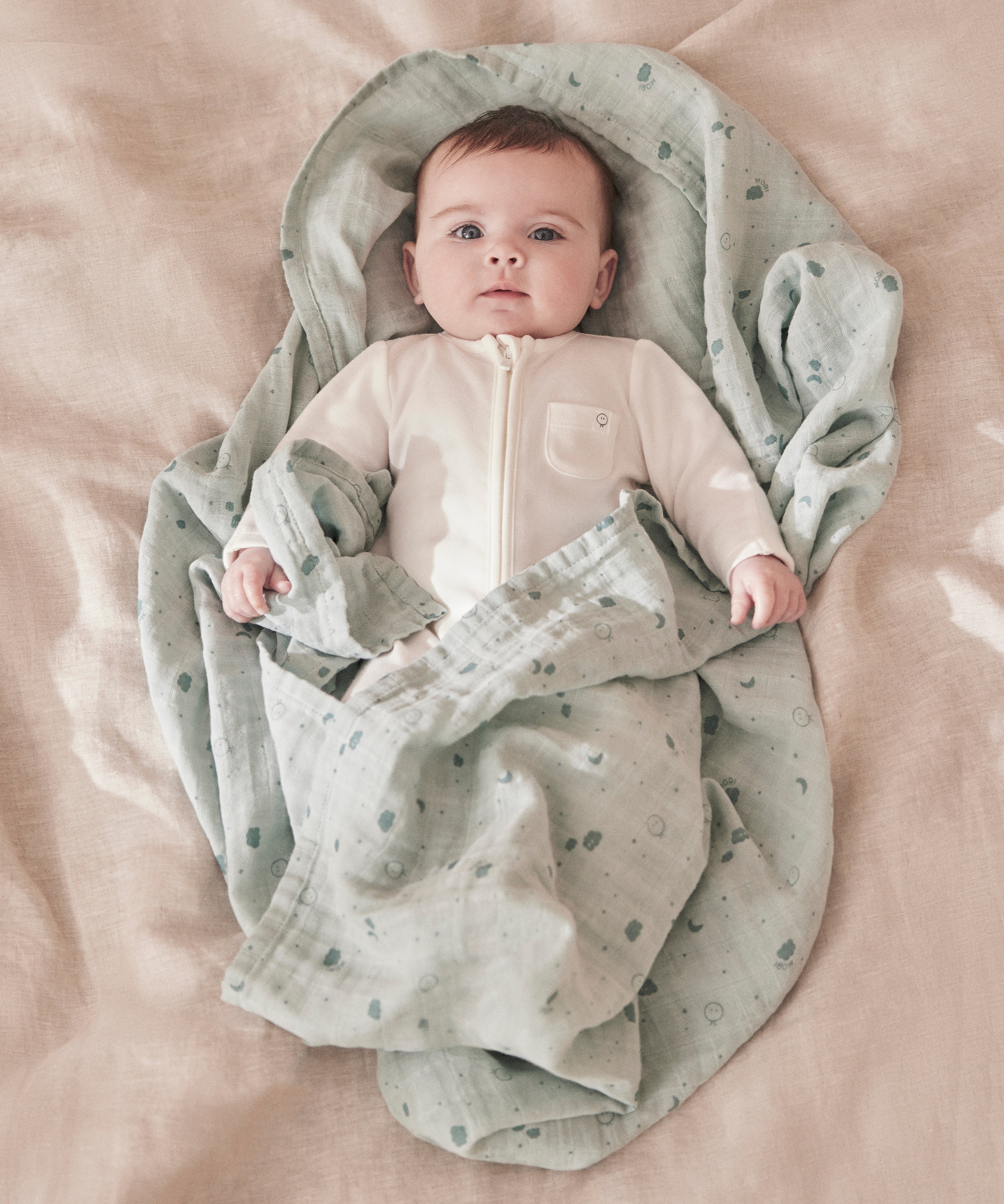 A baby wrapped up in the mint MORI muslin showing the cute print detail on organic cotton fabric