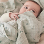 A close up of a baby wrapped up in the mint MORI muslin showing the cute print detail on organic cotton fabric