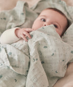 A close up of a baby wrapped up in the mint MORI muslin showing the cute print detail on organic cotton fabric