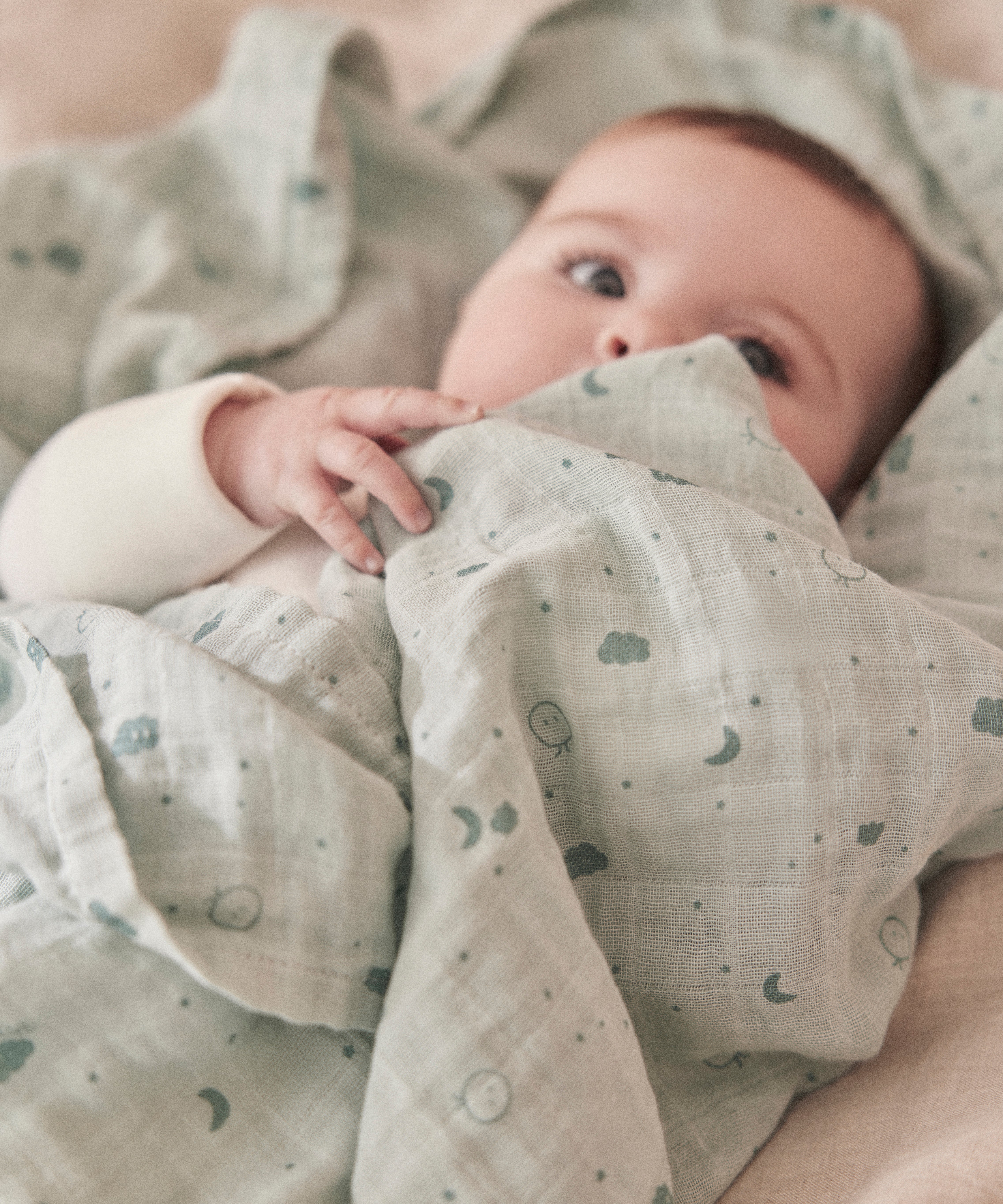 A close up of a baby wrapped up in the mint MORI muslin showing the cute print detail on organic cotton fabric