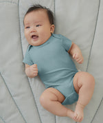 A baby wearing a sky blue Mori organic cotton baby bodysuit with short sleeves.