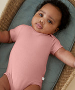 A baby wearing the Mori GOTS organic cotton baby bodysuit in rose pink.