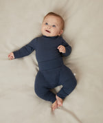 A baby laying on a bed, wearing a matching set of Mori navy comfy joggers made from organic cotton, and a long sleeve top.