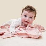 A baby crawling and clutching on the pink MORI muslin square showing the cute white prints of clouds, stars and the moon on organic cotton fabric