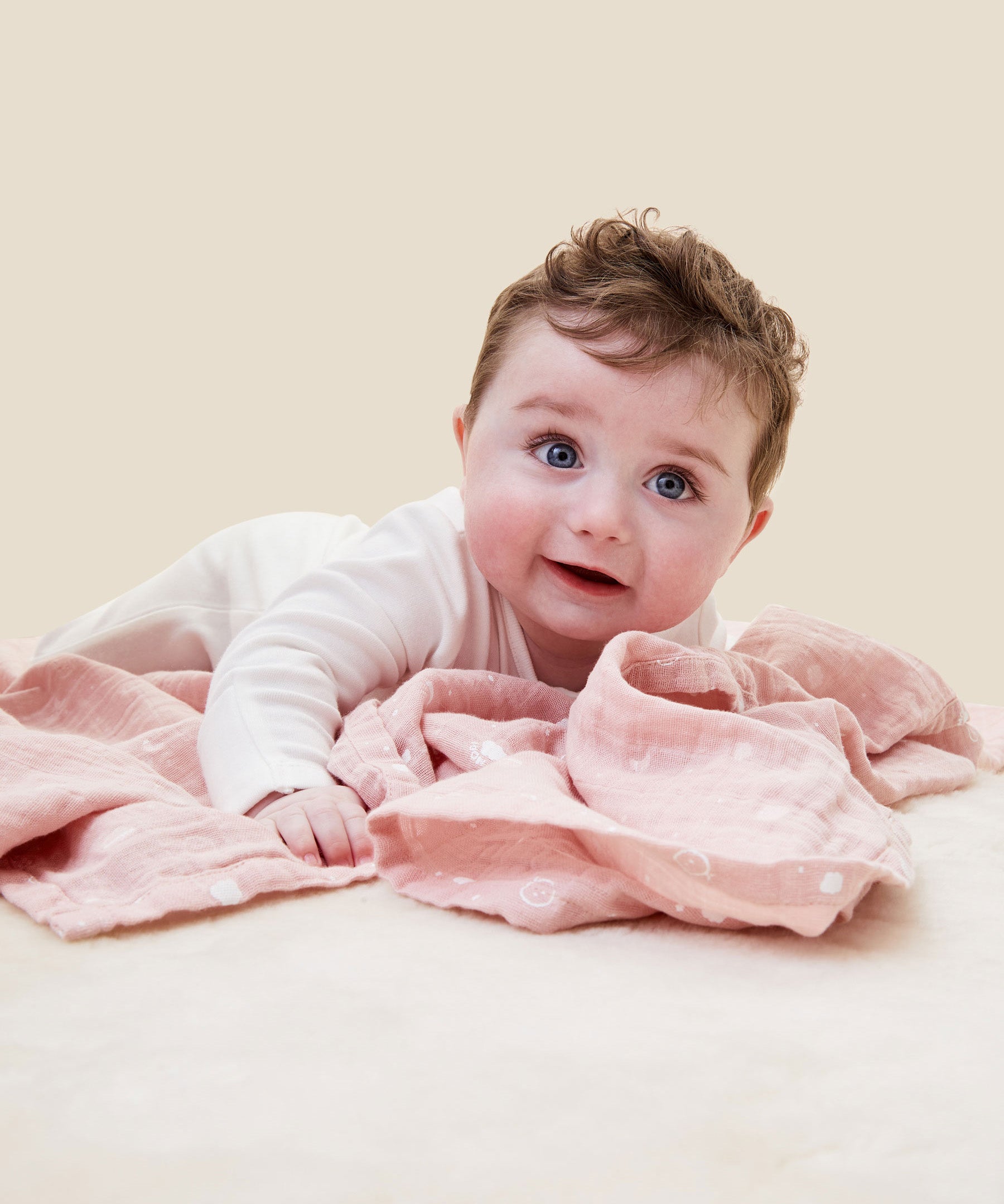 A baby crawling and clutching on the pink MORI muslin square showing the cute white prints of clouds, stars and the moon on organic cotton fabric