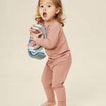 A little girl holding a wooden rainbow stacker toy, and wearing the Mori organic cotton and bamboo blend pyjamas in pink.