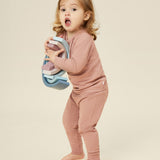 A little girl holding a wooden rainbow stacker toy, and wearing the Mori organic cotton and bamboo blend pyjamas in pink.