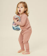 A little girl holding a wooden rainbow stacker toy, and wearing the Mori organic cotton and bamboo blend pyjamas in pink.