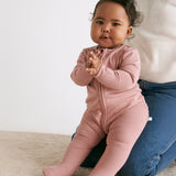 A baby sitting on the mother's knees wearing the MORI two way zip ribbed sleepsuit in rose colour.