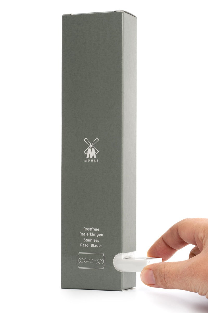 Close up of a hand pulling a small pack of reusable safety razor blades from a large grey box on a white background