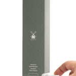 Close up of a hand pulling a small pack of reusable safety razor blades from a large grey box on a white background