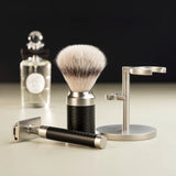 Muhle Rocca black and stainless steel safety razor next to a maching shaving brush with silvertip synthetic fibres and stand