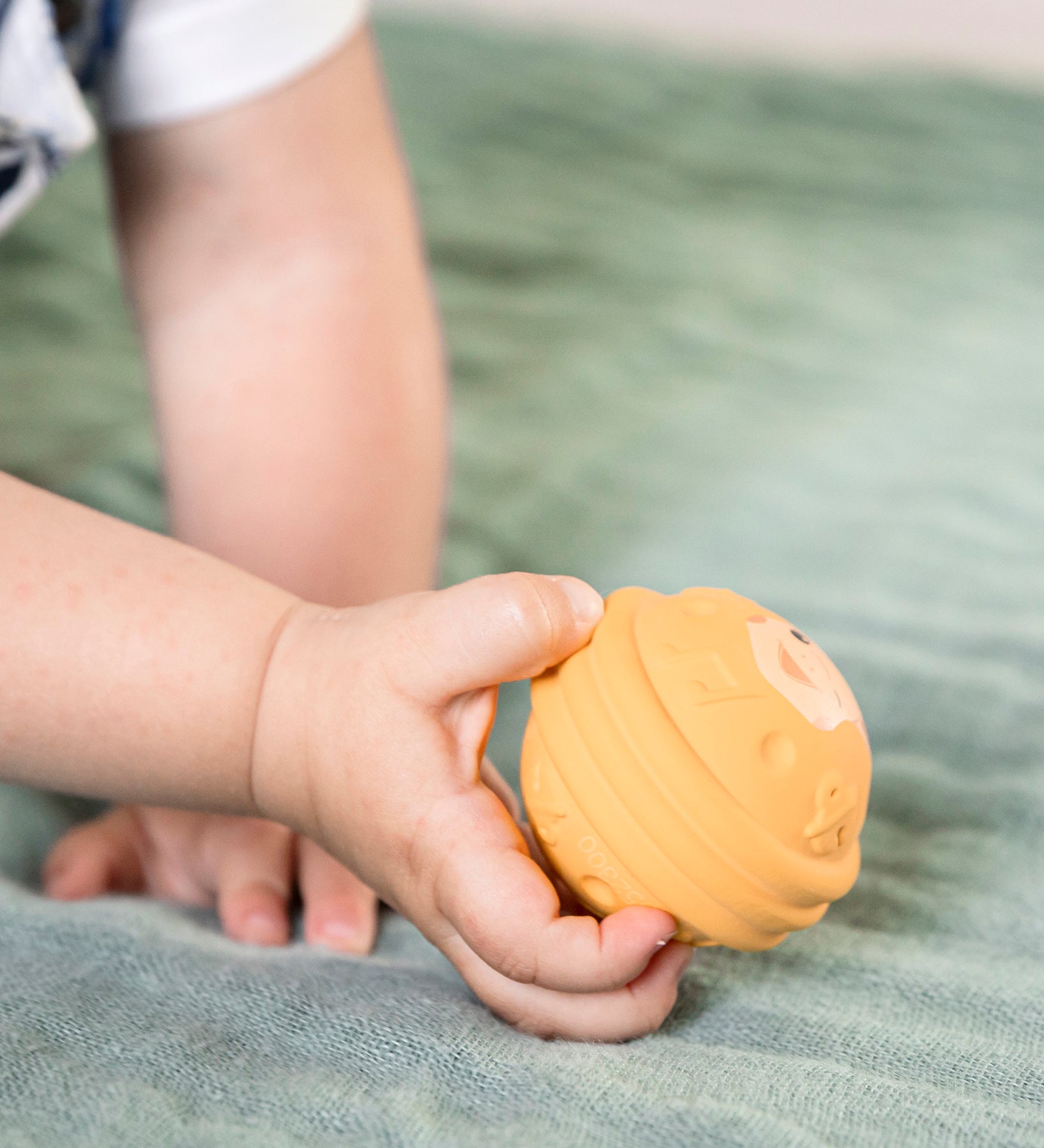 A childs hand holing the yellow ball from the Sophie The Giraffe - Once Upon A Time 5 Senses Musical Balls