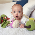 Baby laying on a bed next to some Myum eco-friendly plastic free soft crochet vegetable toys