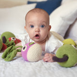 Baby laying on a bed next to some Myum eco-friendly plastic free soft crochet vegetable toys