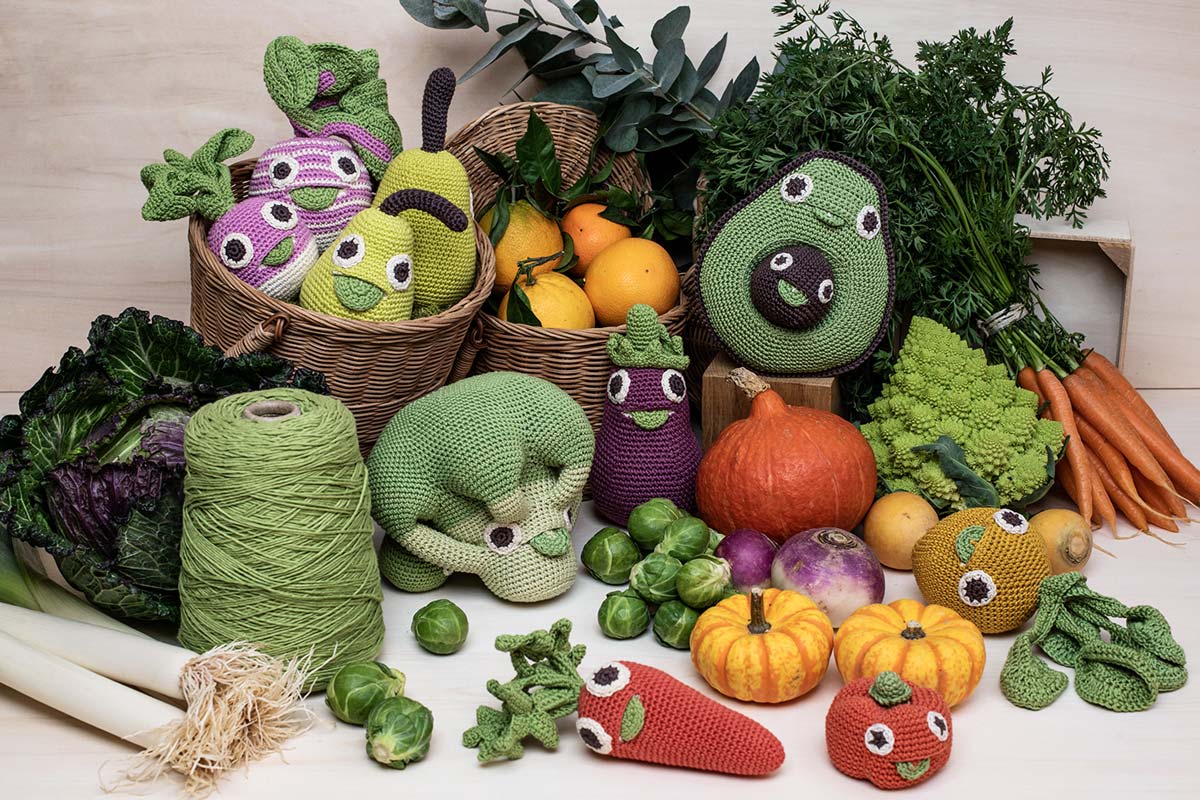 Myum handmade crochet soft vegetable toys laid out on a pile of real vegetables on a white table
