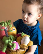 Girl holding a wooden basket full of Myum eco-friendly crochet soft toys on a beige background