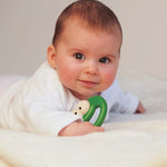 Close up of a baby laying on a bed clutching the Naef Quak eco-friendly wooden baby toy