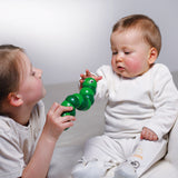 Young girl playing with a green Naef Juba worm toy in front of a baby who is reaching out to hold it.