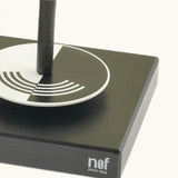 Corner detail of the Naef optical illusion spinning top holder showing a monochrome spinning top sitting on top