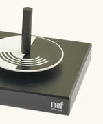 Corner detail of the Naef optical illusion spinning top holder showing a monochrome spinning top sitting on top