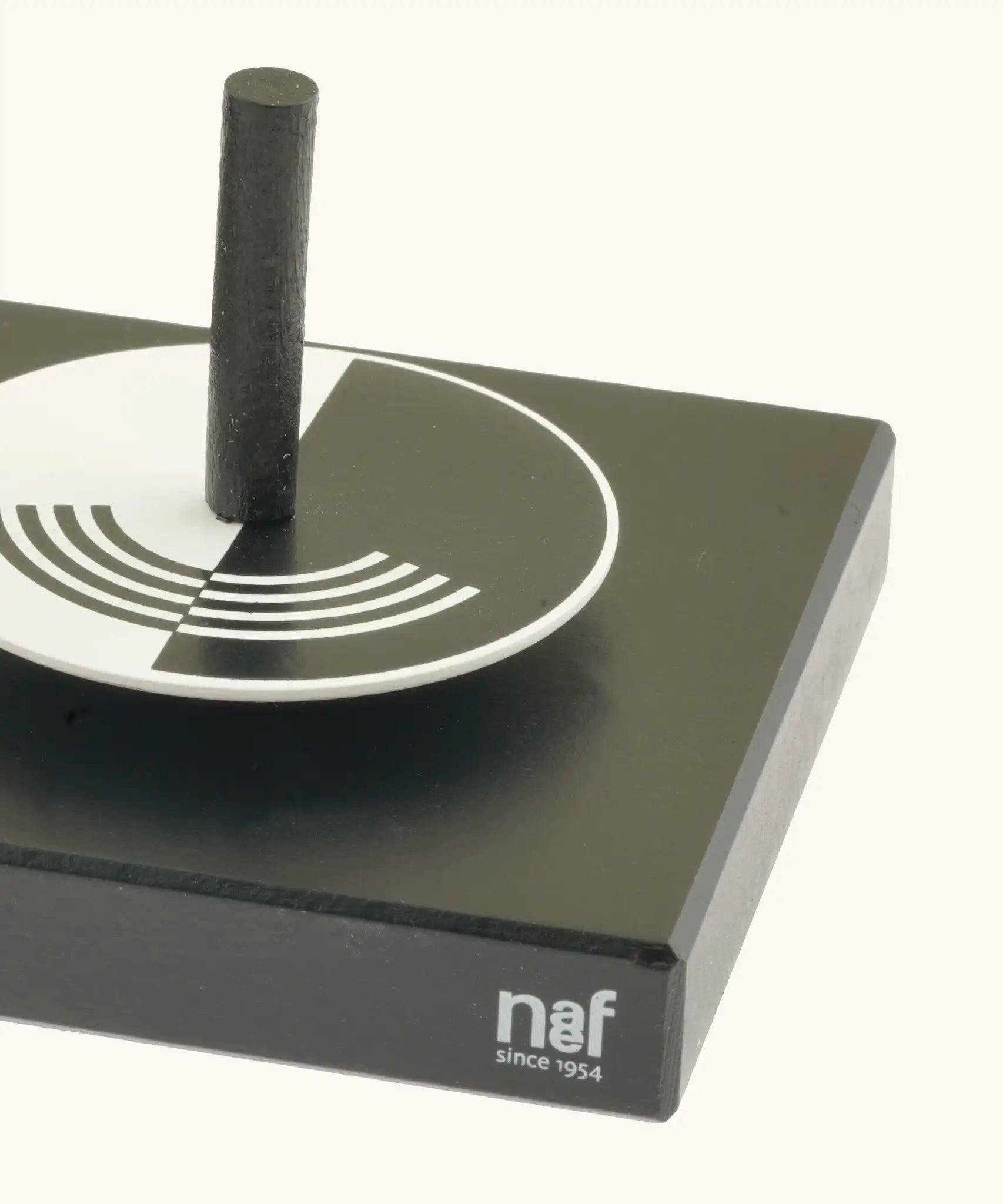 Corner detail of the Naef optical illusion spinning top holder showing a monochrome spinning top sitting on top