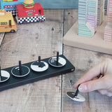 Adult hand holding a single Naef wooden optical illusion spinning top on a wooden surface with vehicles and building blocks in the background