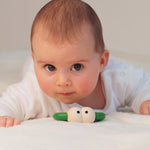 Close up of a baby laying on a bed next to the Naef plastic-free wooden Quak teething toy