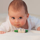 Close up of a baby laying on a bed next to the Naef plastic-free wooden Quak teething toy