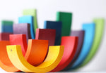 9 piece Naef wooden rainbow stacked on top of each other to form a colourful tower on a white background.