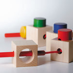 Naef Signa wooden threading toy assembled in a train on a white background. Shows 4 wooden cubes and 4 wooden cylinders with thread weaving through holes in a long curving line.