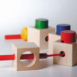Naef Signa wooden threading toy assembled in a train on a white background. Shows 4 wooden cubes and 4 wooden cylinders with thread weaving through holes in a long curving line.