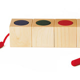 Naef Signa wooden threading toy lined up in a line on a white background. Shows 4 wooden cubes in a line with cylcinders slotted into holes within the cubes. The thread is shown running through all the wooden pieces.