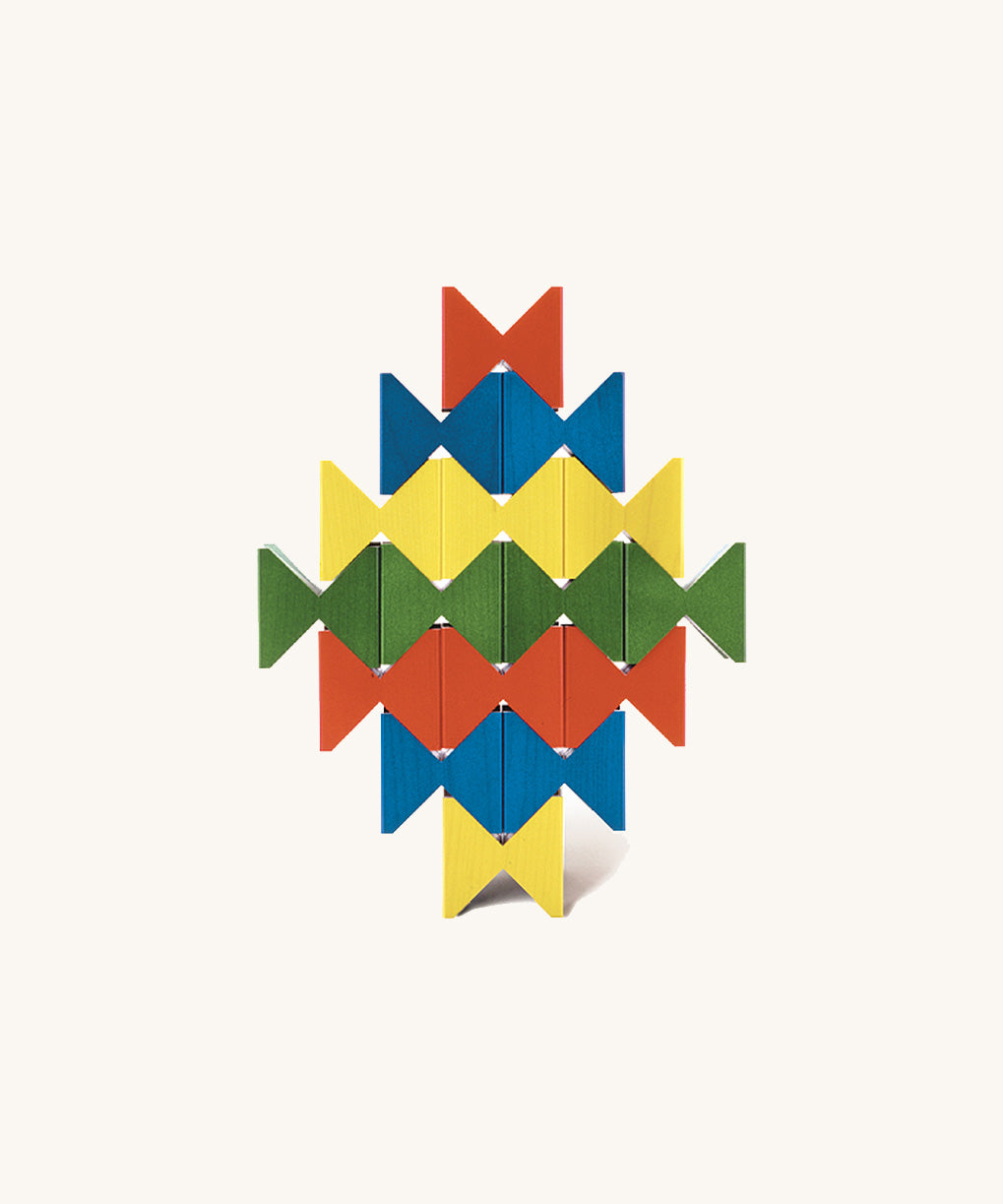 Colourful geometric structure built from Naef Spiel Mini precision wooden blocks in red, blue, yellow, and green. Modern German made wooden puzzle and desk toy.