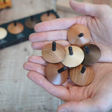 Adult hand holding a collection of loose Naef wooden spinning tops