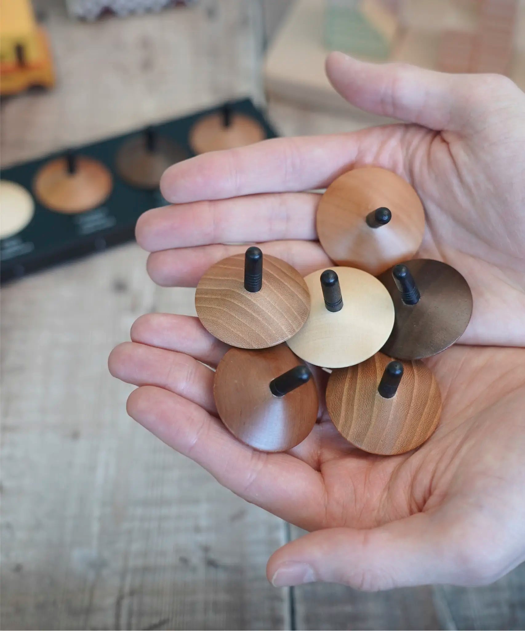 Adult hand holding a collection of loose Naef wooden spinning tops