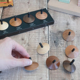 Adult hand holding a loose Naef wooden spinning top by the black stem on a wooden surface next to other spinning tops