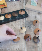 Adult hand holding a loose Naef wooden spinning top by the black stem on a wooden surface next to other spinning tops