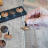 Adult hand holding a loose Naef wooden spinning top by the black stem 