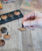 Adult hand holding a loose Naef wooden spinning top by the black stem 