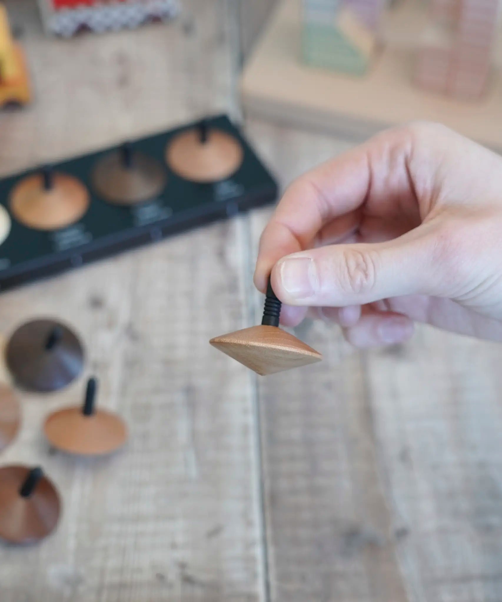 Adult hand holding a loose Naef wooden spinning top by the black stem 