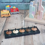 Naef wooden spinning top set sitting on the black holder showing names of different wood with vehicles and blocks in the background.