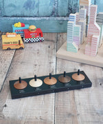 Naef wooden spinning top set sitting on the black holder showing names of different wood with vehicles and blocks in the background.