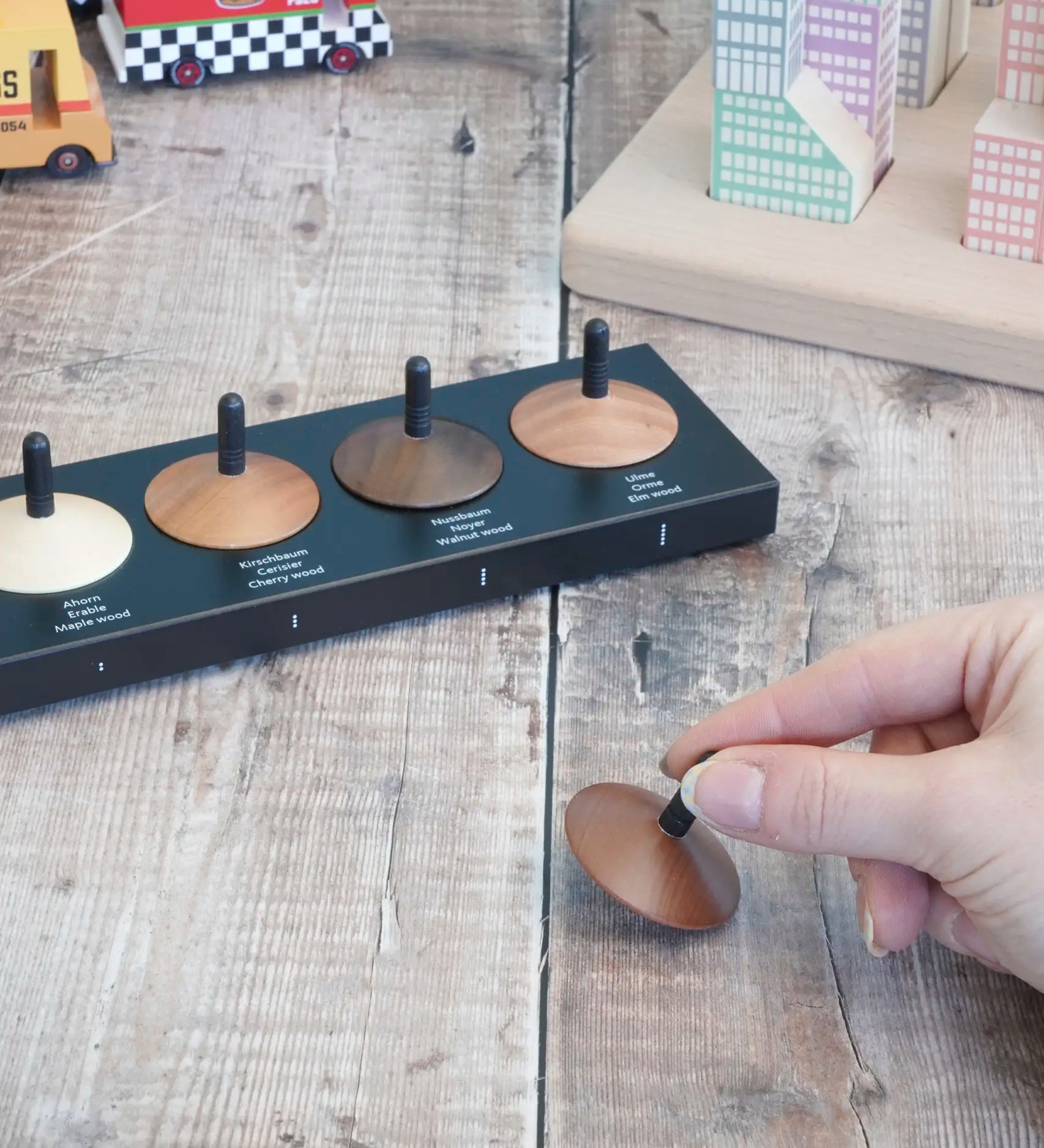 Adult hand holding a loose handcrafted wooden Naef spinning top next to other wooden spinning tops