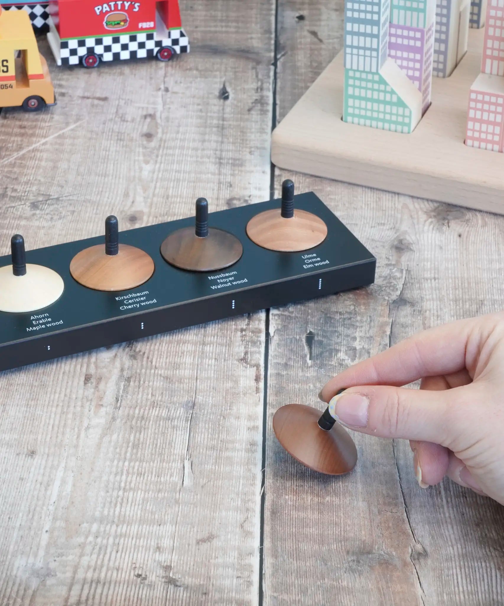 Adult hand holding a loose handcrafted wooden Naef spinning top next to other wooden spinning tops