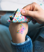 A closeup of a child's hand, applying a Namaki non-toxic temporary butterfly tattoo. 