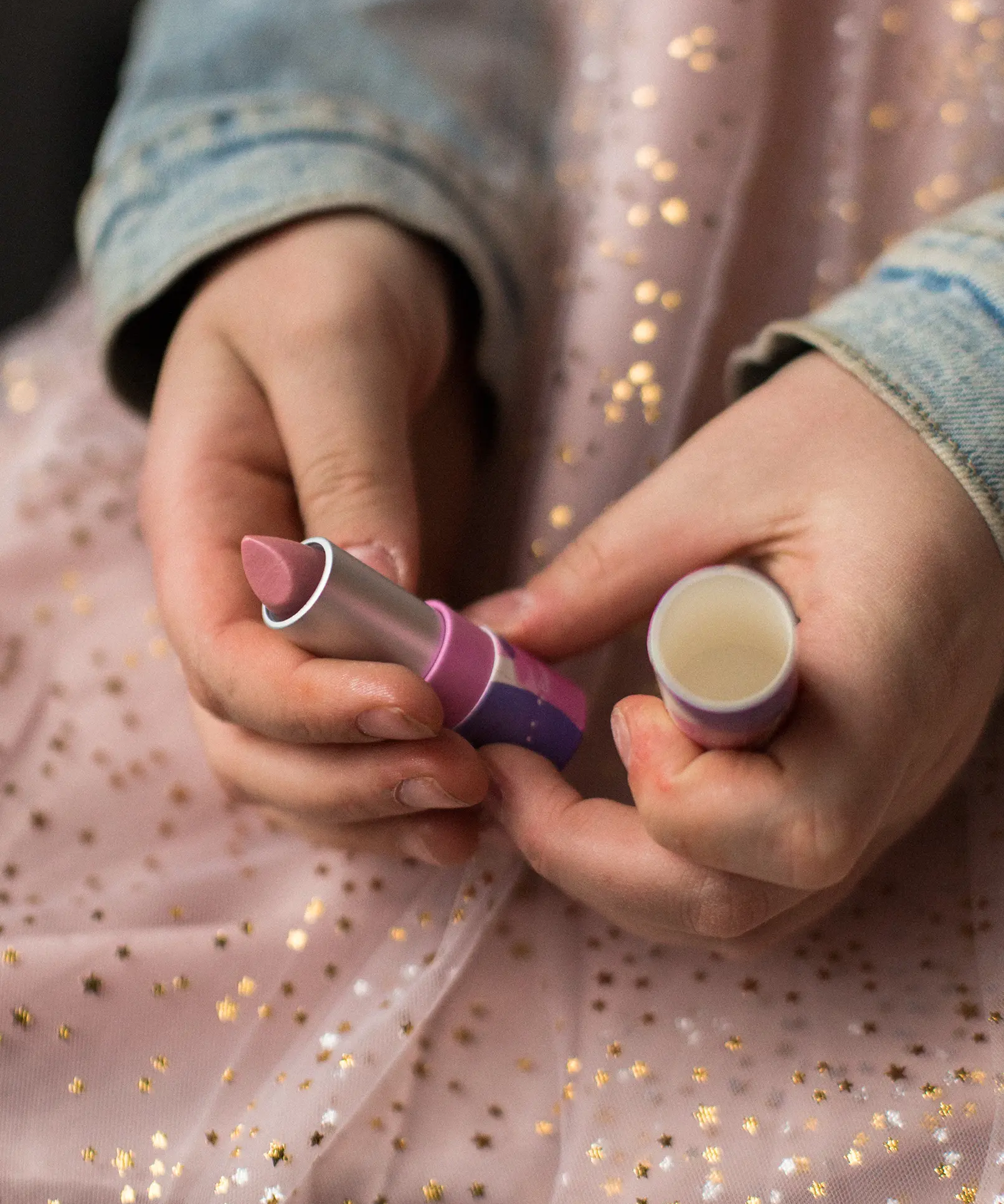 A closeup of a child's hands holding the Namaki natural kids' raspberry lip balm from the Nightingale makeup giftset