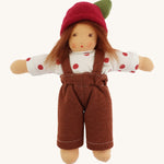 A beautiful Waldorf, handmade doll with a white top with red spots, a brown pair of dungarees, light brown hair and a red apple hat with a green leaf. On a cream background